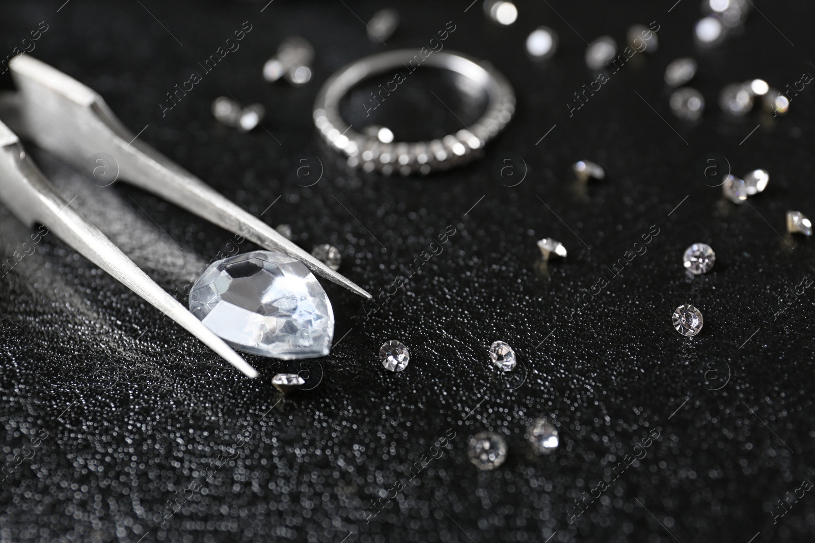 Photo of Jewels and tweezers on black leather surface