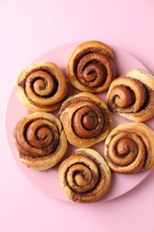 Many tasty cinnamon rolls pink background, top view