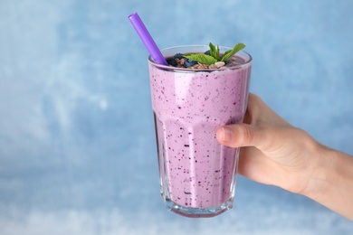 Woman holding glass of delicious blueberry smoothie on blue background, closeup