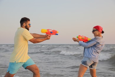 Happy couple playing with water guns near sea at sunset