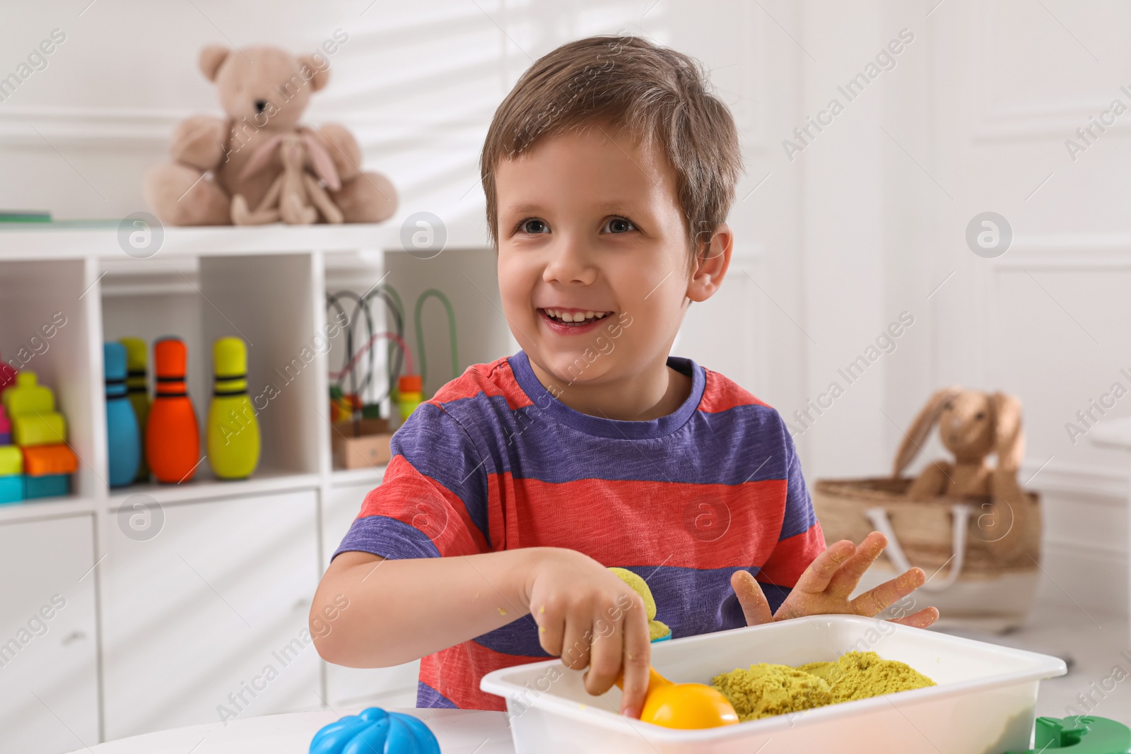 Photo of Cute little boy playing with bright kinetic sand at table in room