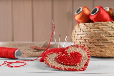 Photo of Heart of burlap fabric with red stitches and spools of threads on white wooden table. Space for text