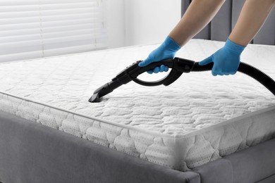 Woman disinfecting mattress with vacuum cleaner indoors, closeup