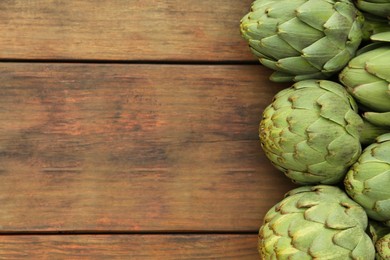 Many fresh raw artichokes on wooden table, flat lay. Space for text