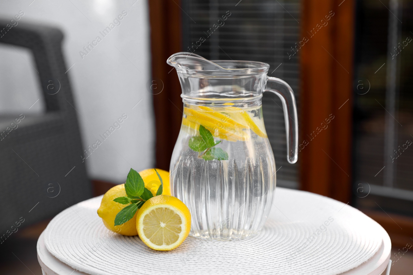 Photo of Jug of water with lemons and mint on white table outdoors