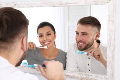 Photo of Young couple cleaning teeth against mirror in bathroom
