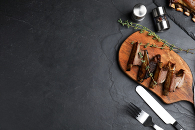 Photo of Delicious roasted ribs served on black table, flat lay. Space for text