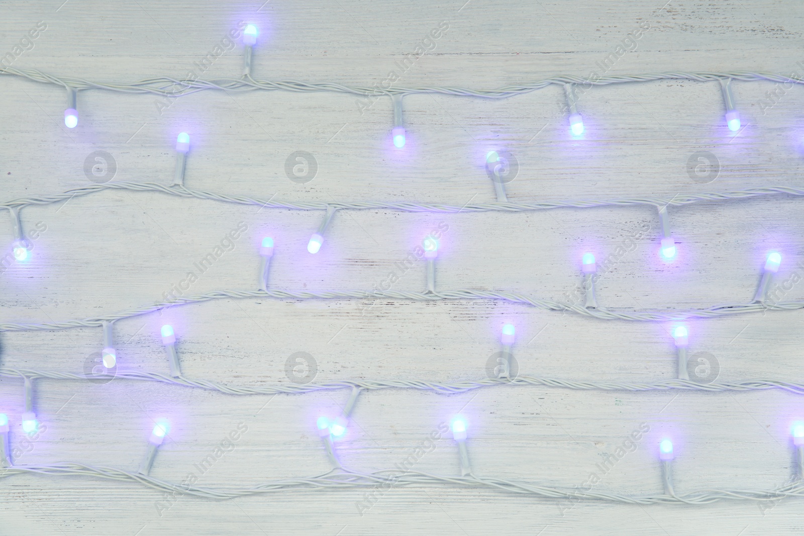 Photo of Glowing Christmas lights on wooden background, top view