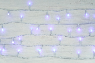 Photo of Glowing Christmas lights on wooden background, top view