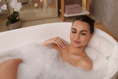 Photo of Young woman using pillow while enjoying bubble bath indoors