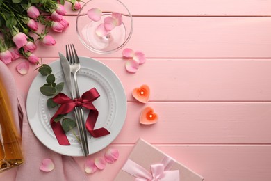 Photo of Place setting with heart shaped candles, bouquet of roses and gift for romantic dinner on pink wooden table, flat lay. Space for text