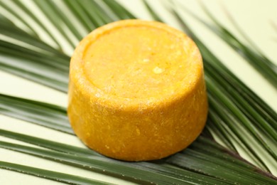 Photo of Orange solid shampoo bar and leaf on green background, closeup. Hair care