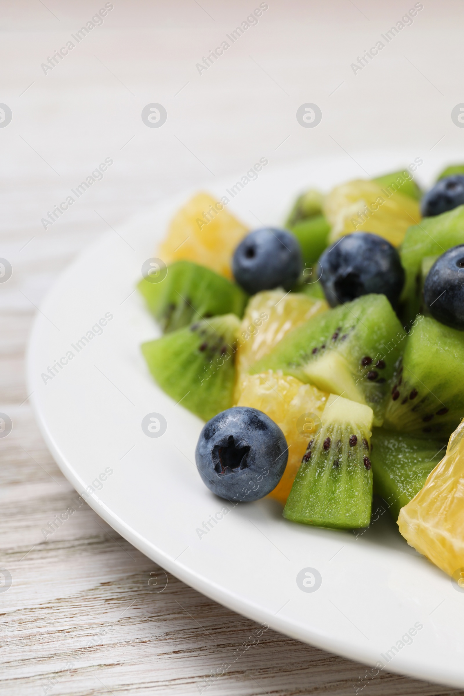 Photo of Plate of tasty fruit salad on white wooden table, closeup