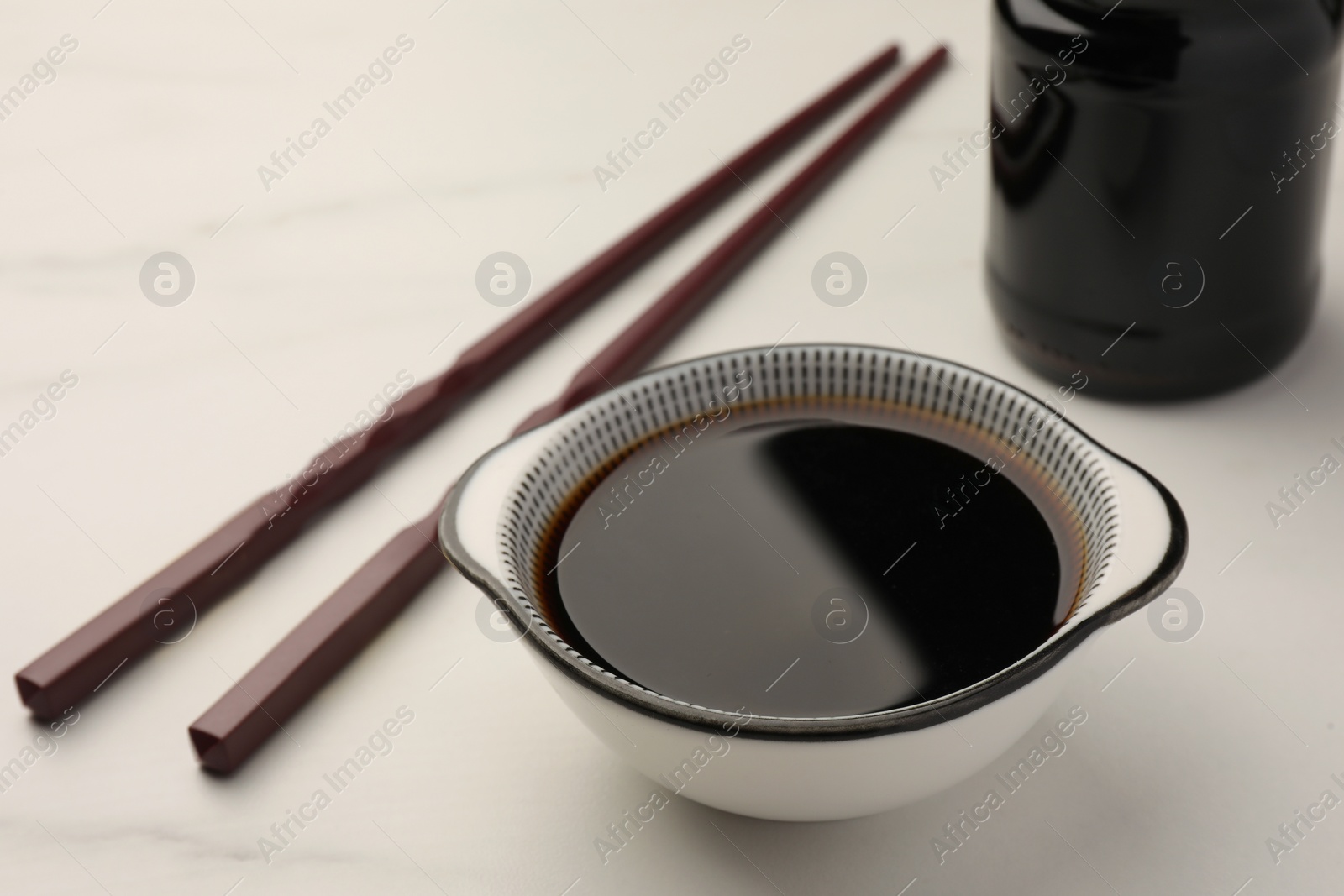 Photo of Bowl with soy sauce and chopsticks on white table, closeup