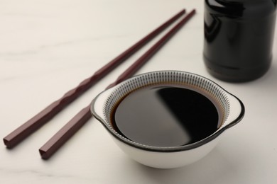 Bowl with soy sauce and chopsticks on white table, closeup