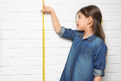 Photo of Little girl measuring her height on brick wall background