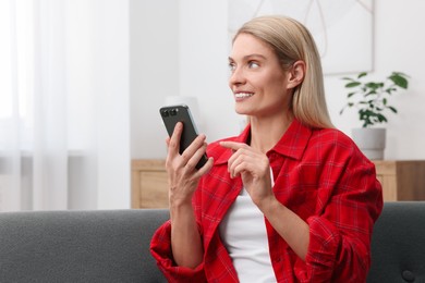 Woman sending message via smartphone at home, space for text