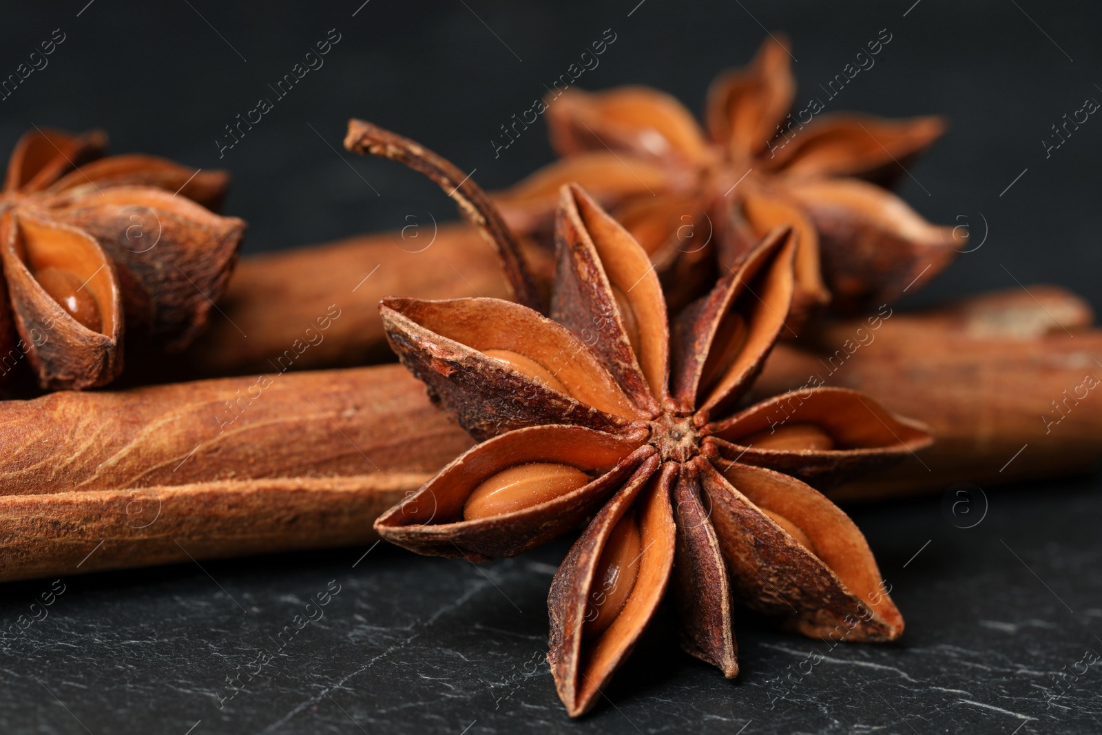 Photo of Aromatic anise stars and cinnamon sticks on black table, closeup