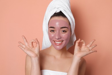 Woman with pomegranate face mask showing Ok on pale coral background