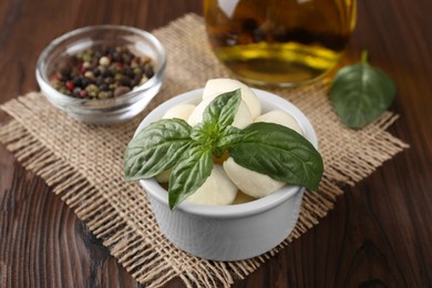 Tasty mozarella balls and basil leaves in bowl on wooden table, closeup