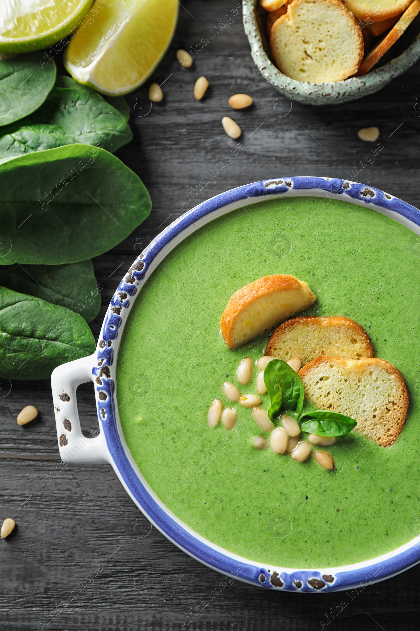 Photo of Bowl of healthy green soup with fresh spinach on grey wooden table, flat lay