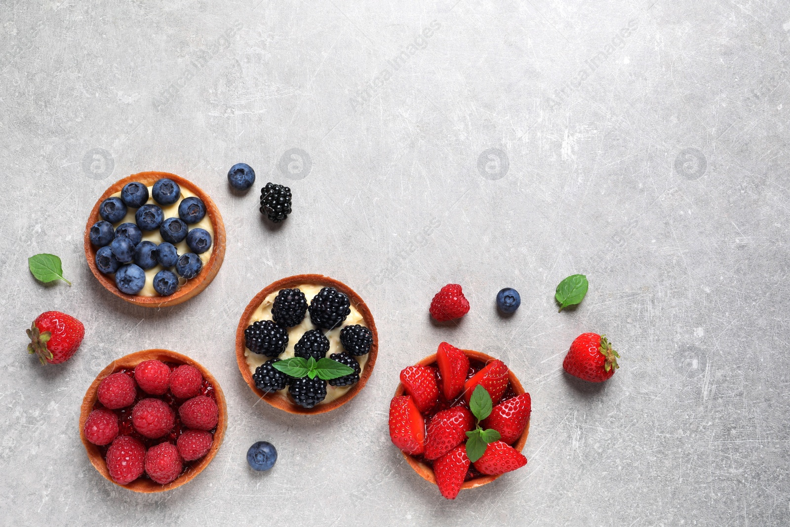 Photo of Tartlets with different fresh berries on light grey table, flat lay and space for text. Delicious dessert