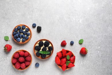 Tartlets with different fresh berries on light grey table, flat lay and space for text. Delicious dessert