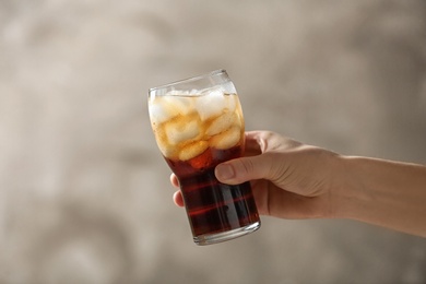 Woman holding glass of cola with ice on color background, closeup. Space for text