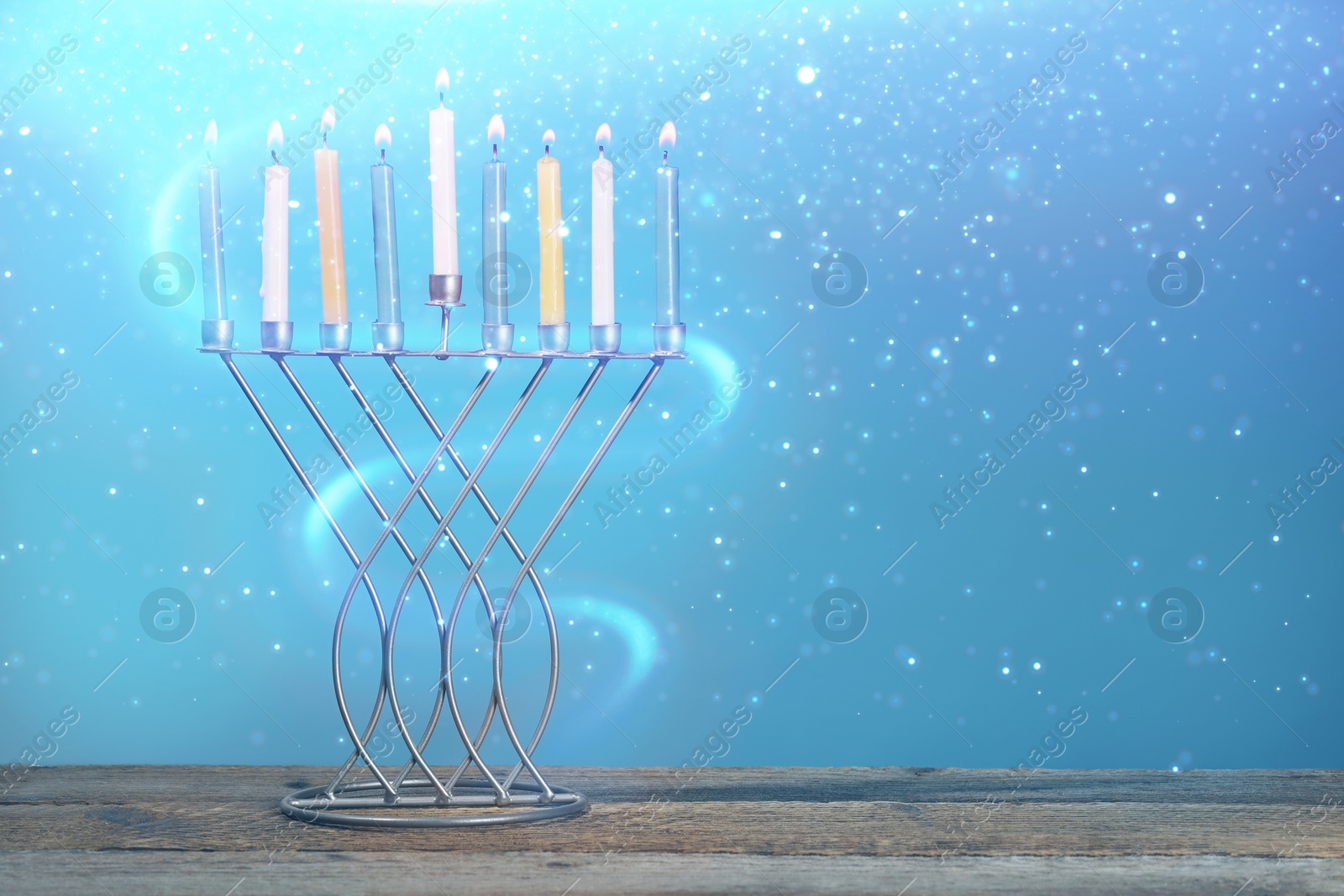 Image of Hanukkah celebration. Menorah with burning candles on wooden table against light blue background, space for text