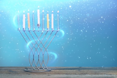 Hanukkah celebration. Menorah with burning candles on wooden table against light blue background, space for text