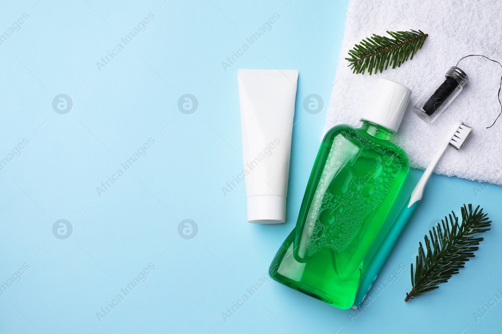 Photo of Fresh mouthwash in bottle, toothbrush, toothpaste and dental floss on light blue background, flat lay. Space for text