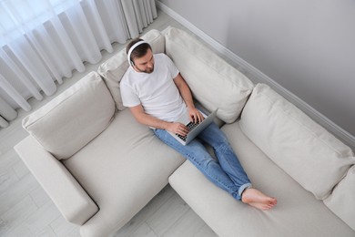 Man with laptop and headphones sitting on sofa at home