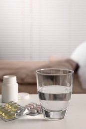 Photo of Glass of water, different pills in blisters and medical bottle on white table indoors