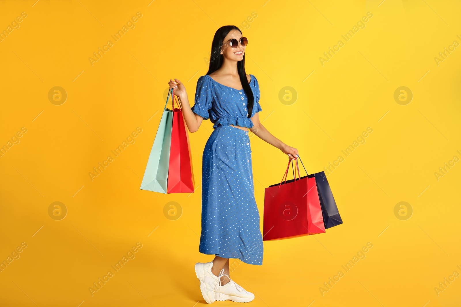 Photo of Beautiful young woman with paper shopping bags on yellow background