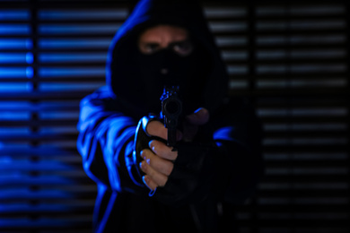 Dangerous criminal in mask near window indoors, focus on gun