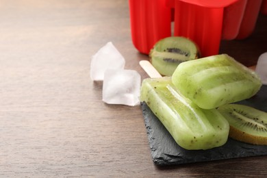 Photo of Tasty kiwi ice pops on wooden table, space for text. Fruit popsicle
