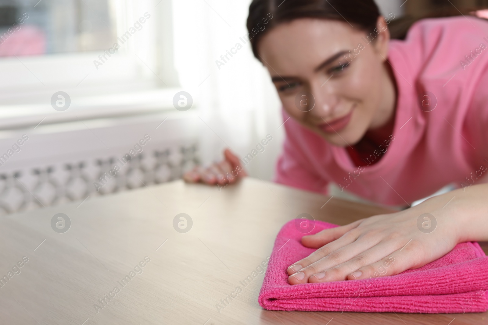 Photo of Young woman cleaning wooden table with rag at home, focus on hand. Space for text