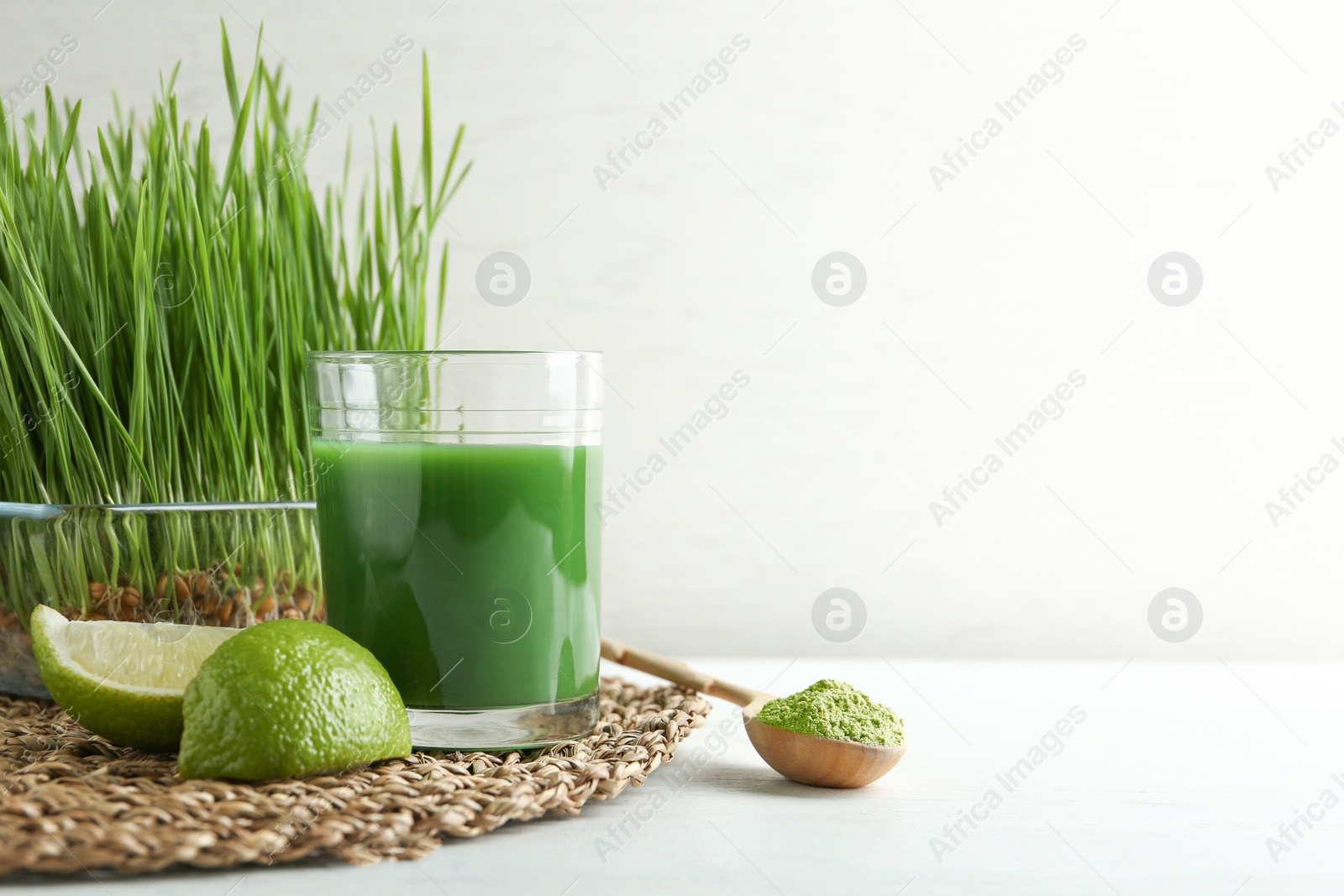 Composition with glass of wheat grass juice and lime on table against light background. Space for text Photo of Composition with glass of wheat grass juice and lime on table against light background. Space for text