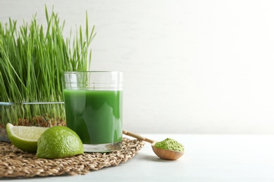 Photo of Composition with glass of wheat grass juice and lime on table against light background. Space for text
