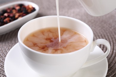 Pouring milk into cup with aromatic tea at table, closeup