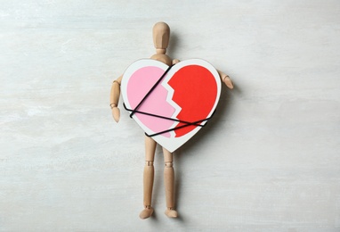 Photo of Wooden puppet with symbol of broken heart on gray background, top view. Relationship problems
