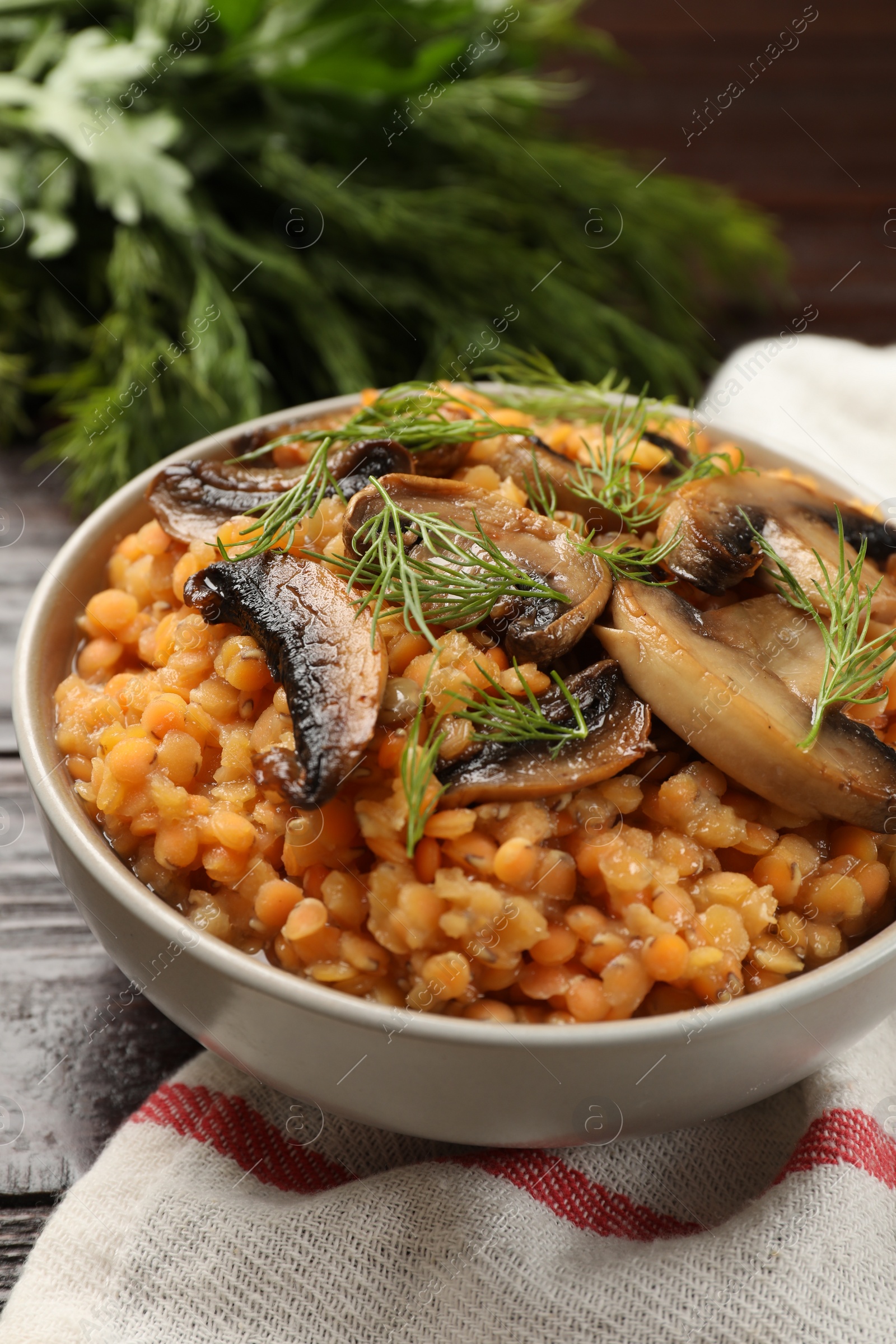 Photo of Delicious red lentils with mushrooms and dill in bowl on table, closeup