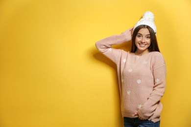 Beautiful young woman in warm sweater with hat on color background. Space for text