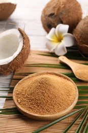 Photo of Coconut sugar, palm leaves, fruits and bamboo mat on wooden rustic table, closeup