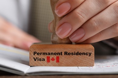 Image of Woman stamping document at wooden table, closeup. Permanent residency visa in Canada