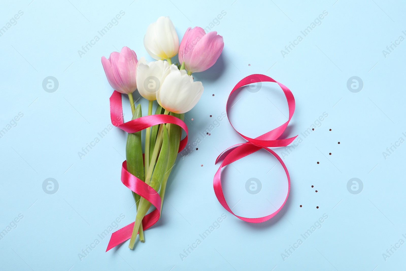 Photo of 8th of March greeting card design with pink ribbon and beautiful flowers on light blue background, flat lay. International Women's day