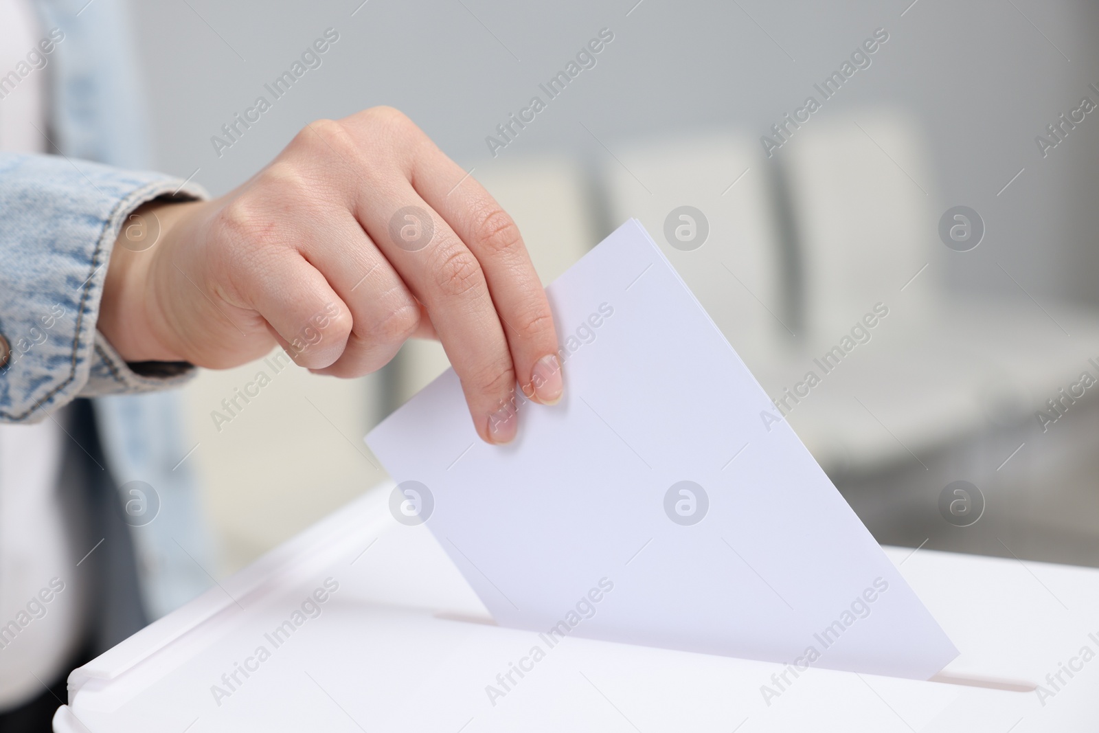 Photo of Woman putting her vote into ballot box on blurred background, closeup