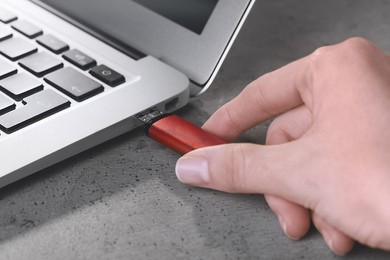 Photo of Woman attaching usb flash drive into laptop at light grey table, closeup