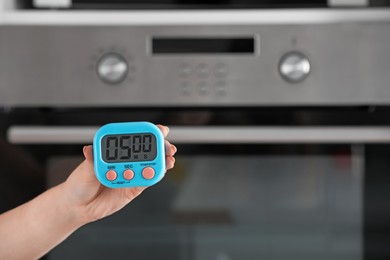 Photo of Woman holding digital kitchen timer near oven, closeup. Space for text