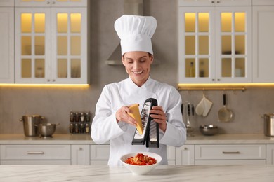 Photo of Professional chef grating cheese into delicious dish at white marble table in kitchen